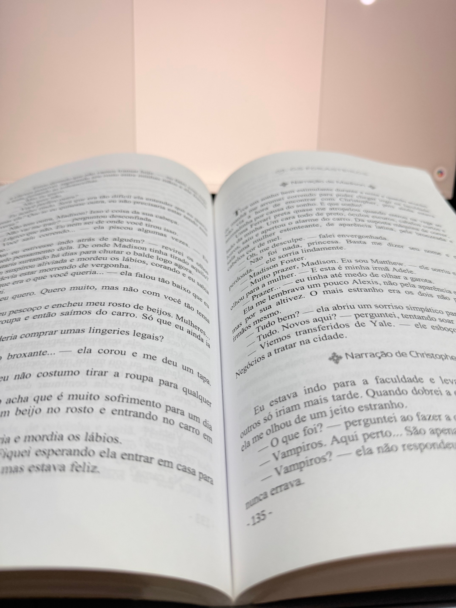 Foto real de outro livro físico aberto mostrando páginas diagramadas e narração destacada